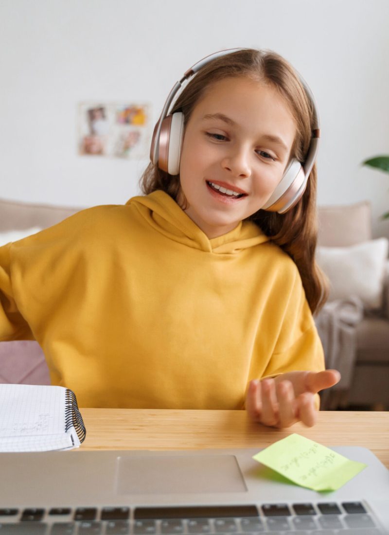 Cheerful girl with headphones sitting at her room, talking on camera, having video call, using laptop computer for communicate with friends or classmates, shooting video for her followers. Webcam view
