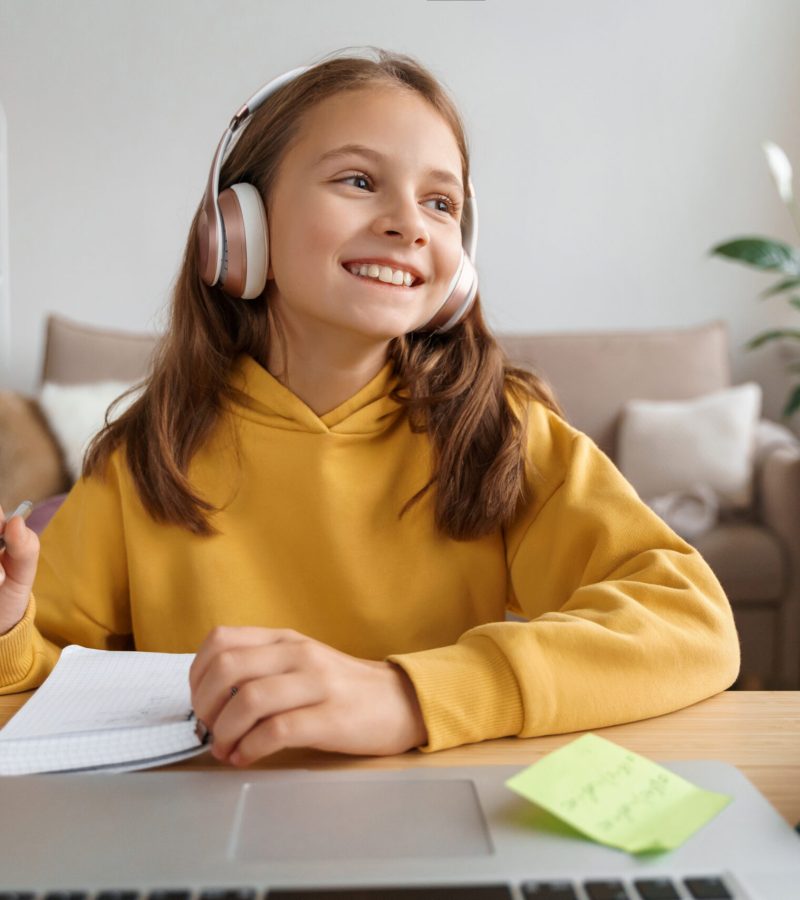 Happy girl wearing headphones using laptop for learning from home during coronavirus pandemic, enjoys her remote education, having online lesson with school teacher. Distant studying, homeschooling
